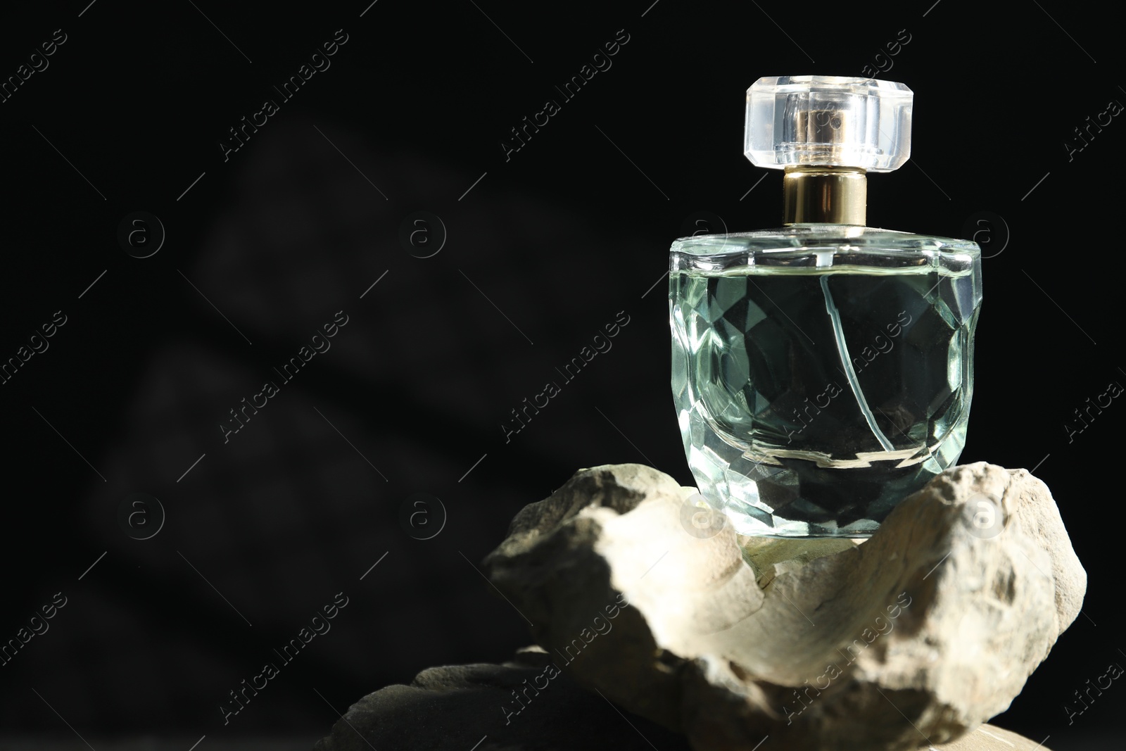 Photo of Bottle of fragrant perfume on rock against dark background, space for text