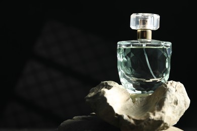 Photo of Bottle of fragrant perfume on rock against dark background, space for text