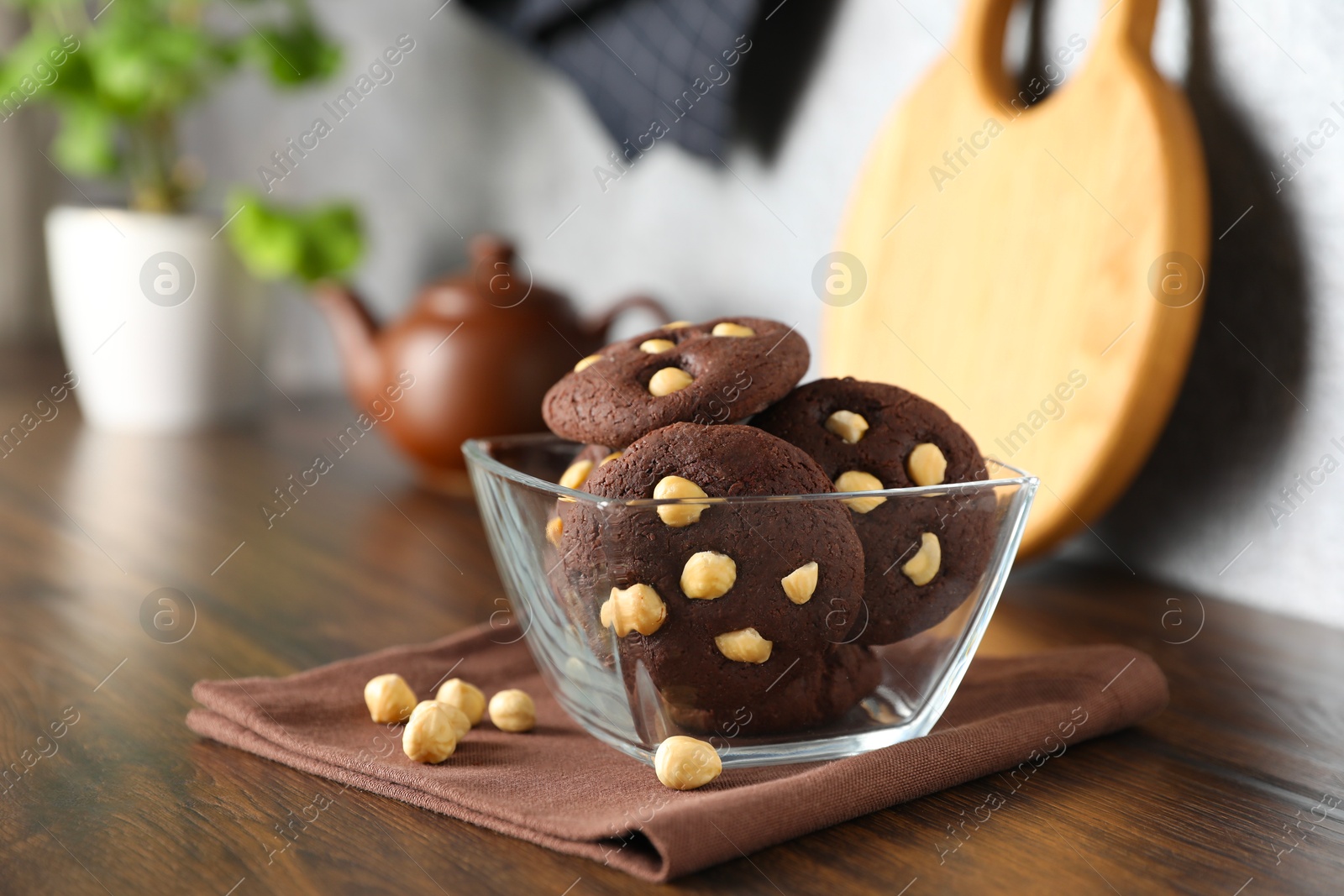 Photo of Tasty chocolate cookies with hazelnuts in bowl on wooden table, closeup