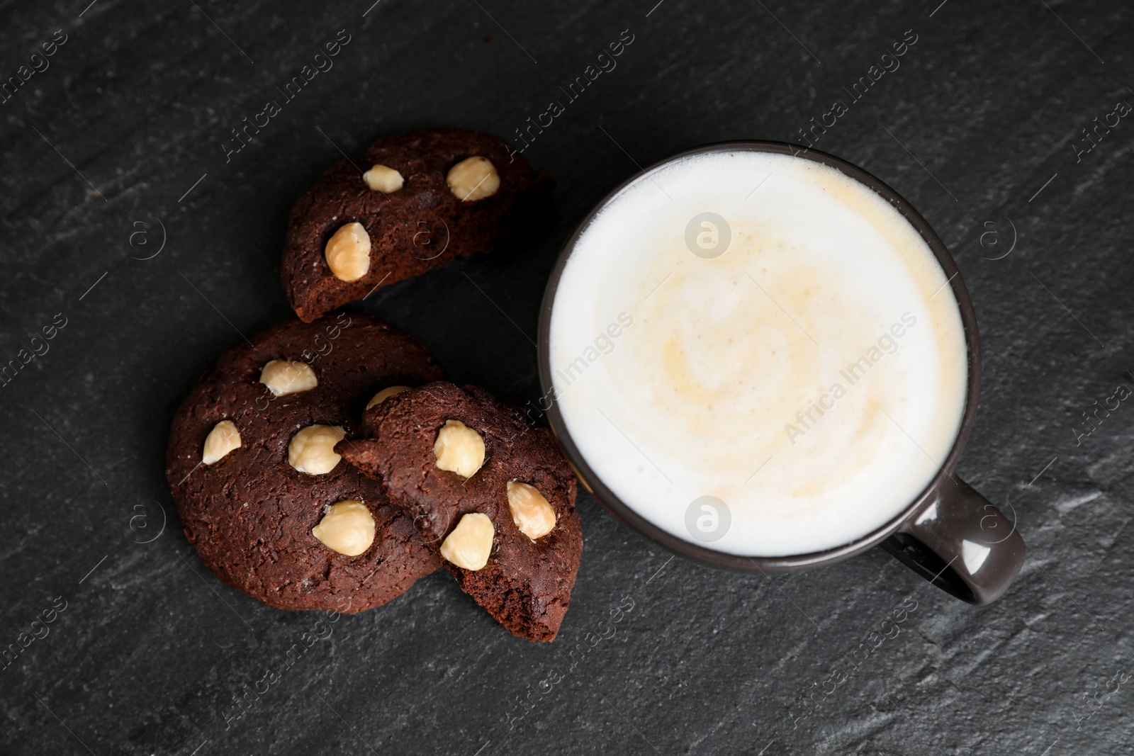 Photo of Tasty chocolate cookies with hazelnuts and coffee on black table, flat lay