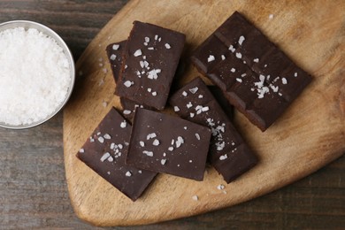 Photo of Pieces of chocolate with salt on wooden table, top view