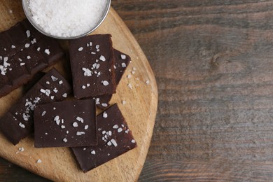 Photo of Pieces of chocolate with salt on wooden table, top view. Space for text