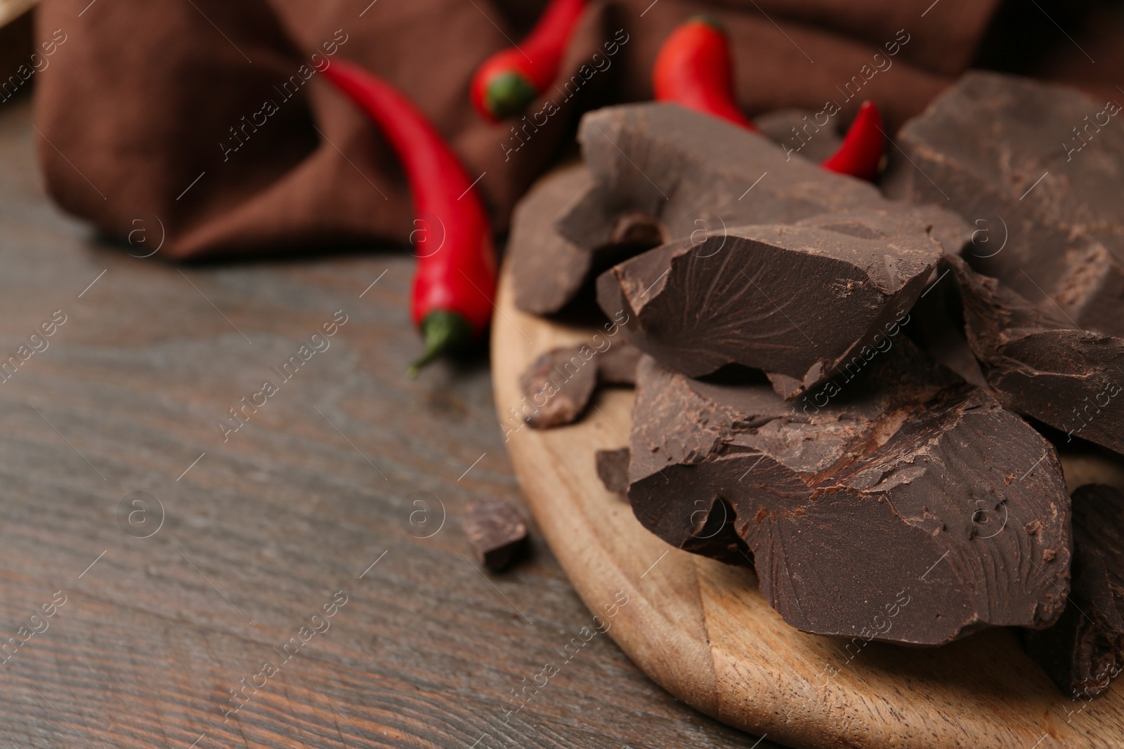 Photo of Pieces of chocolate with chili peppers on wooden table, closeup. Space for text