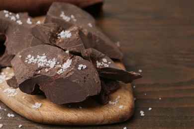 Photo of Pieces of chocolate with salt on wooden table, closeup. Space for text