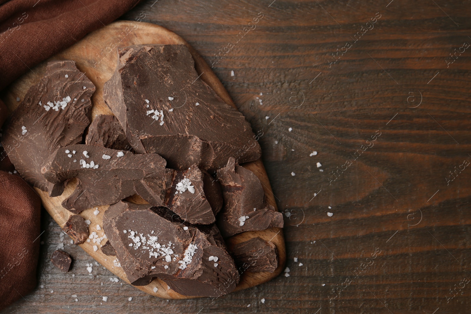 Photo of Pieces of chocolate with salt on wooden table, top view. Space for text