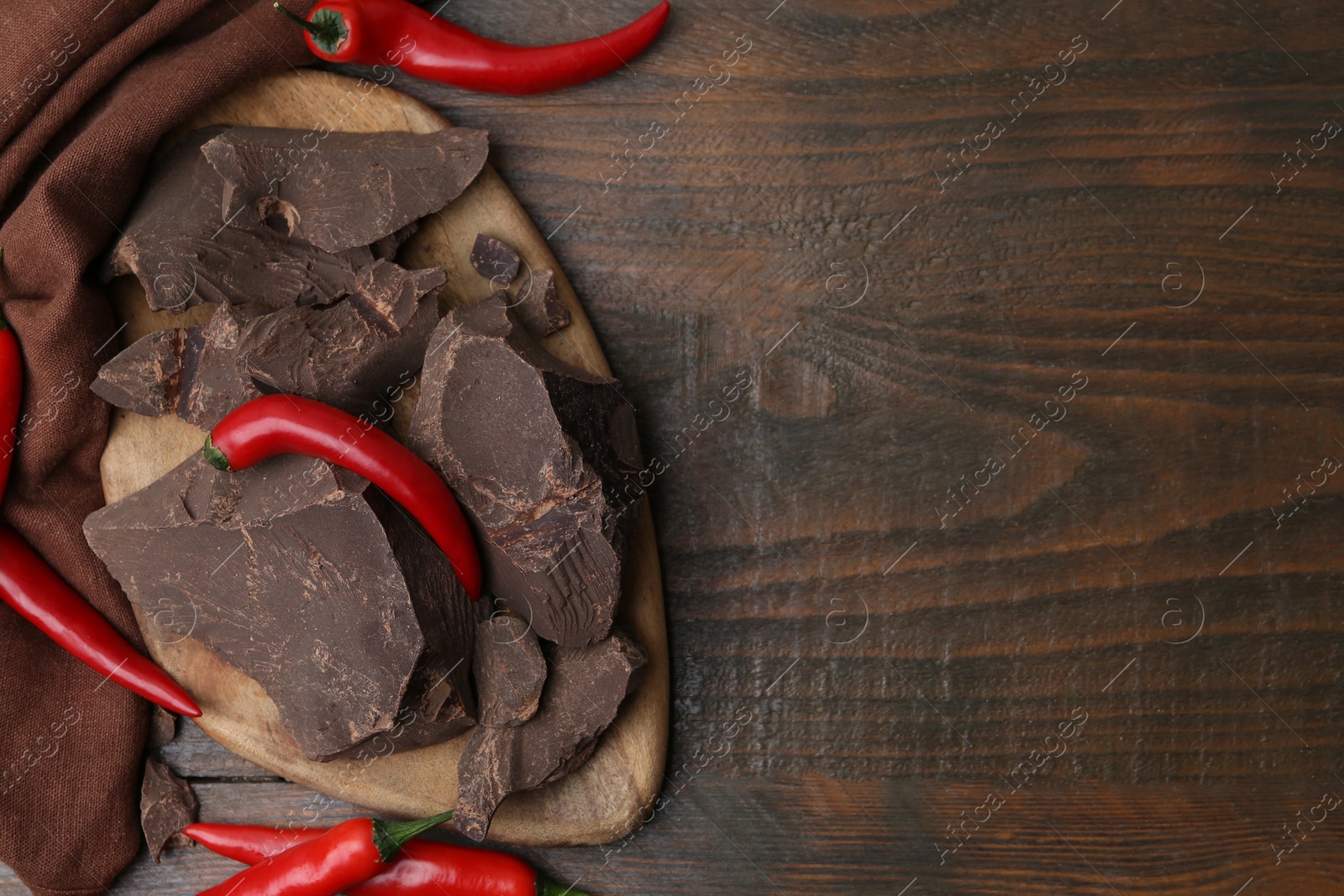 Photo of Pieces of chocolate with chili peppers on wooden table, flat lay. Space for text