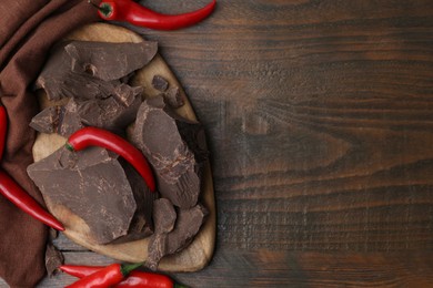 Photo of Pieces of chocolate with chili peppers on wooden table, flat lay. Space for text