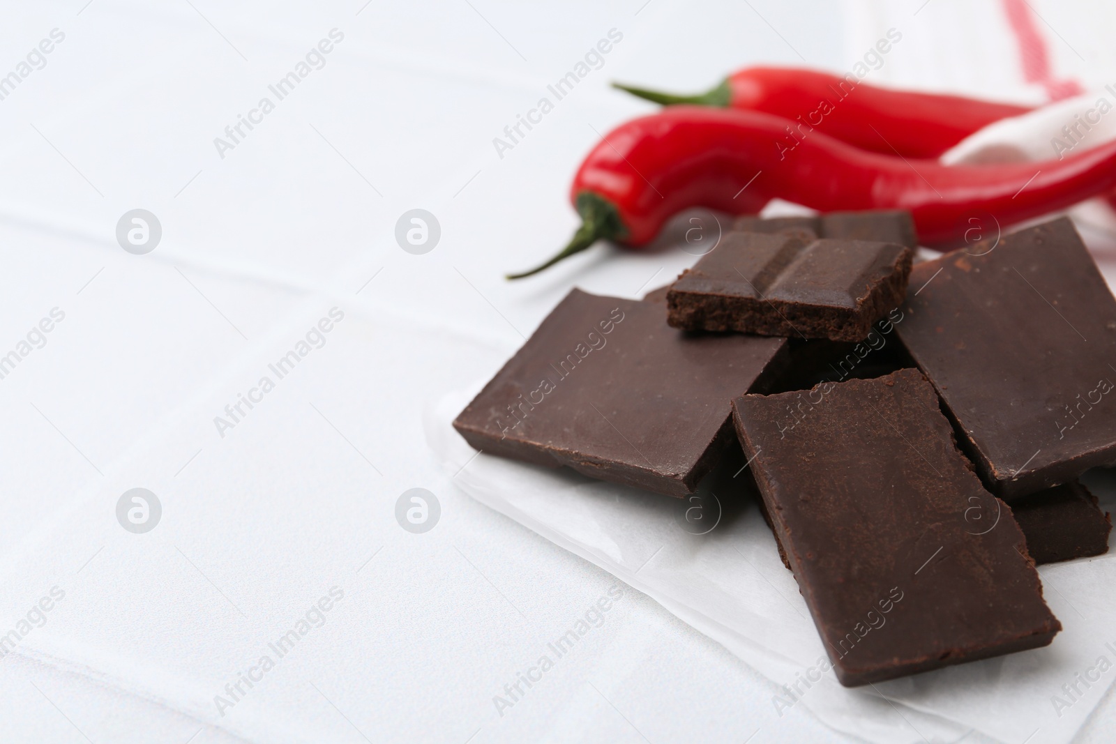 Photo of Pieces of chocolate with chili peppers on white table, closeup. Space for text