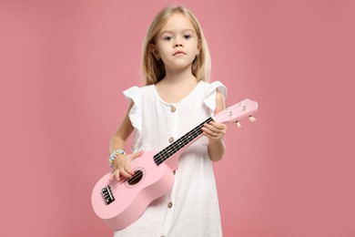 Photo of Little girl playing ukulele on pink background