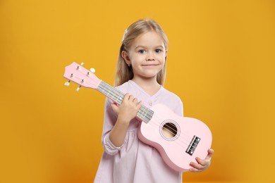 Photo of Little girl with ukulele on orange background