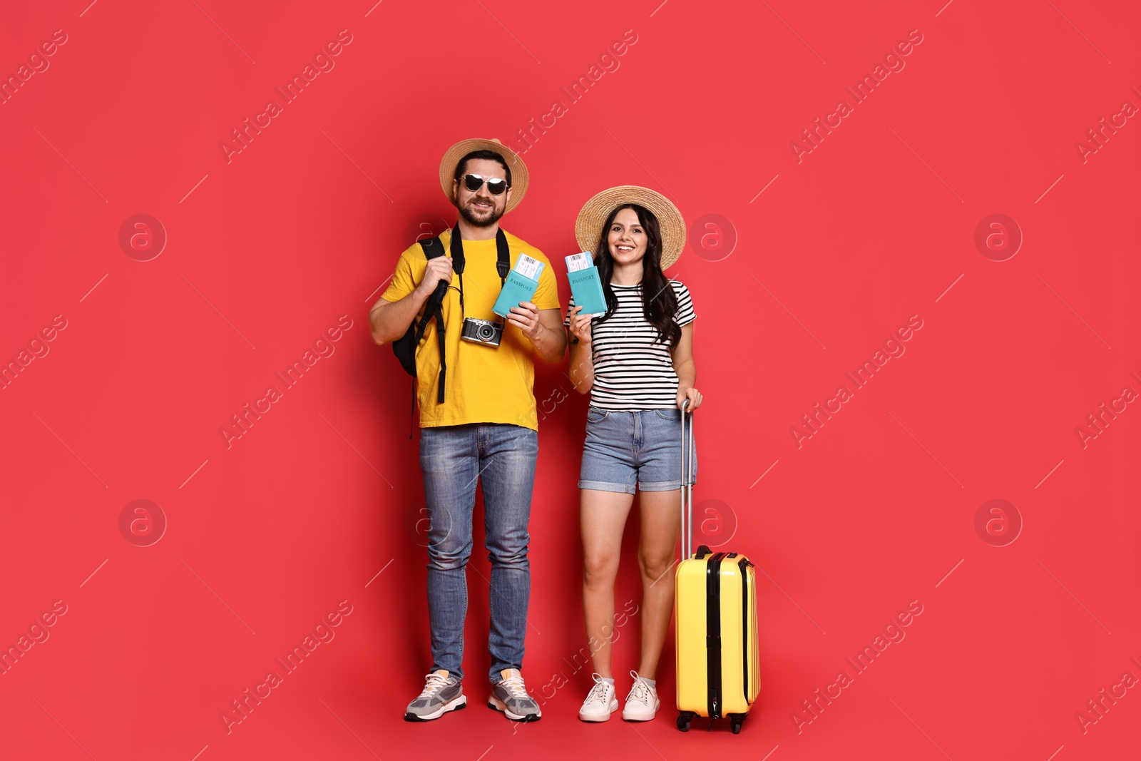 Photo of Tourism. Happy couple in hats with suitcase, passports and tickets on red background