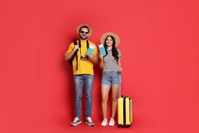 Photo of Tourism. Happy couple in hats with suitcase, passports and tickets on red background