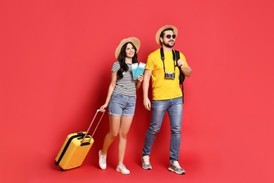 Photo of Tourism. Happy couple in hats with suitcase, passports and tickets on red background