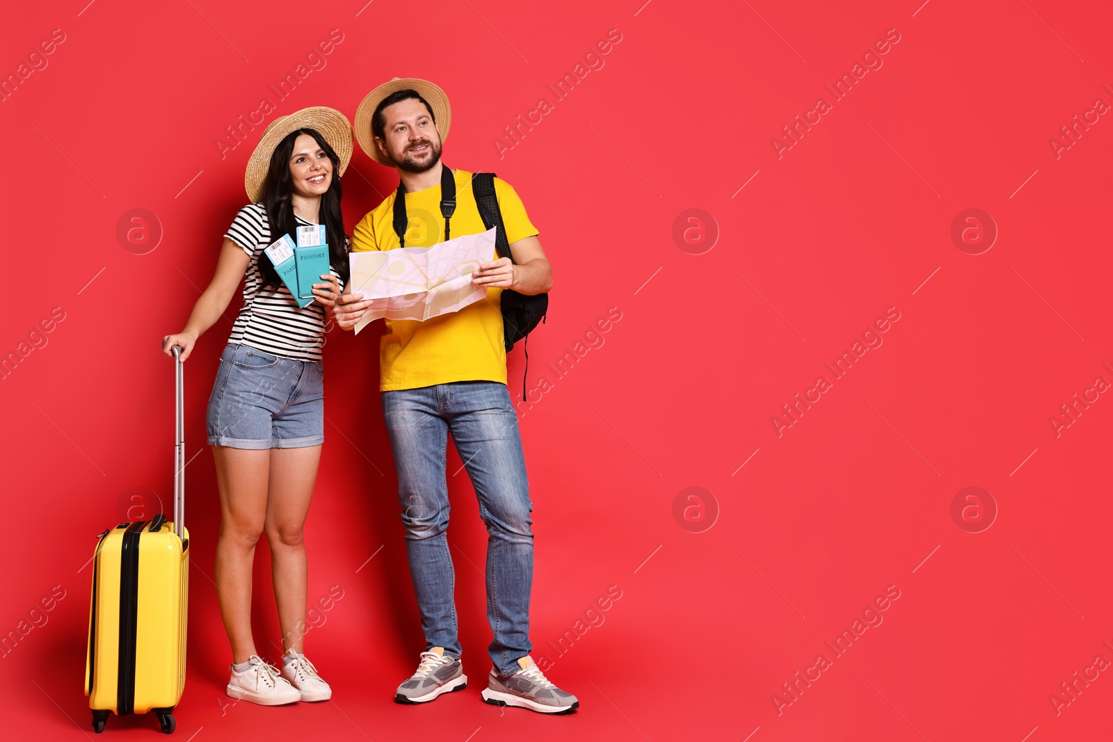 Photo of Tourism. Happy couple in hats with suitcase, passports and tickets on red background