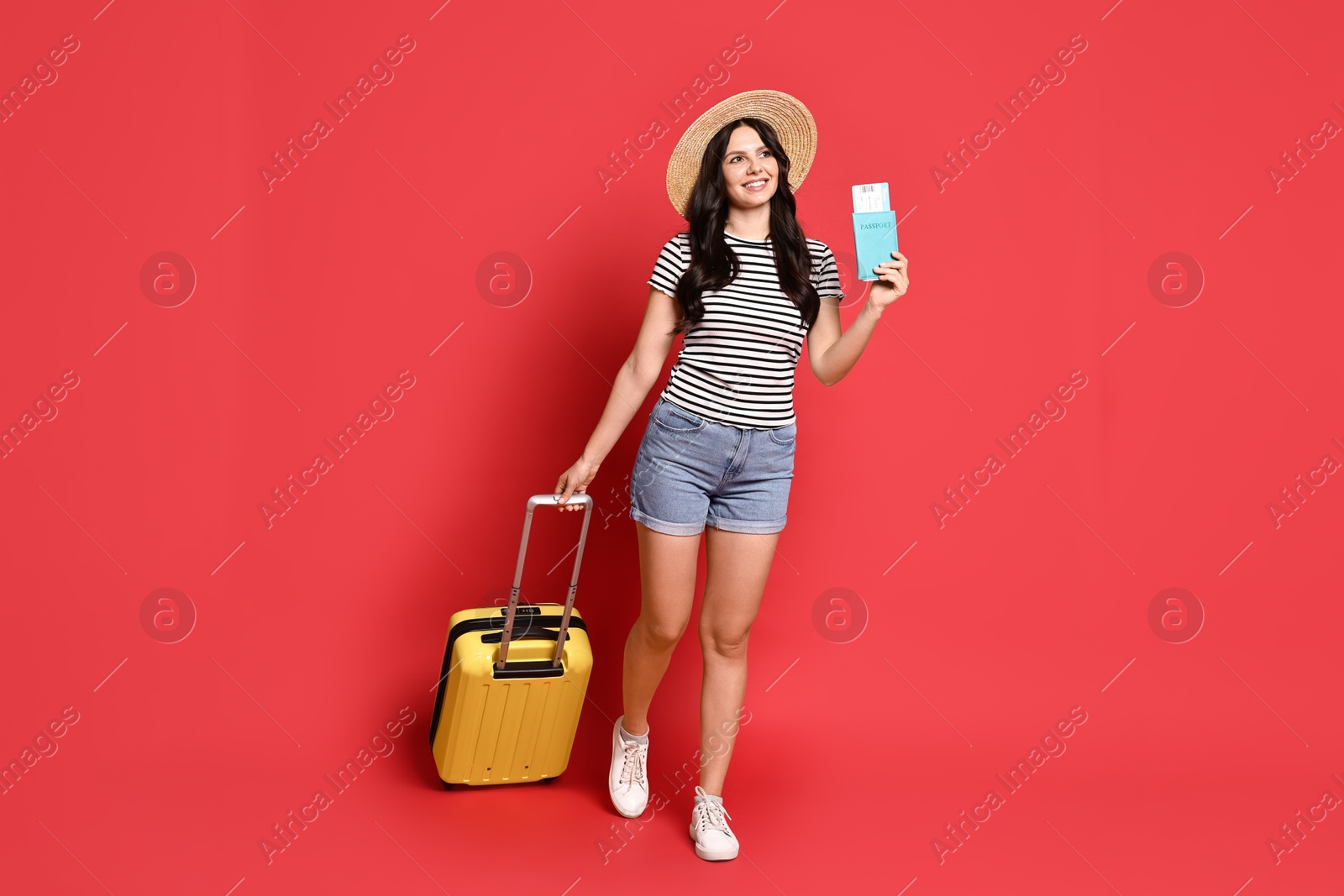 Photo of Young tourist in hat with suitcase, passport and ticket on red background