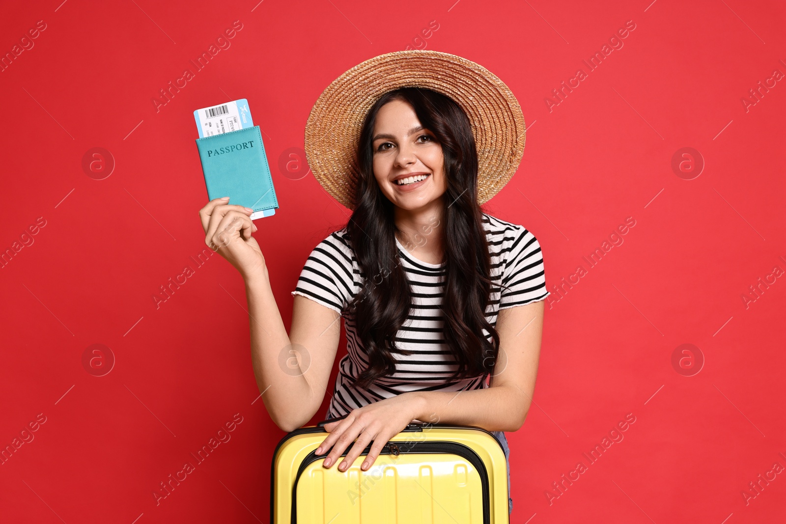 Photo of Young tourist in hat with suitcase, passport and ticket on red background