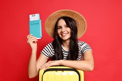 Photo of Young tourist in hat with suitcase, passport and ticket on red background