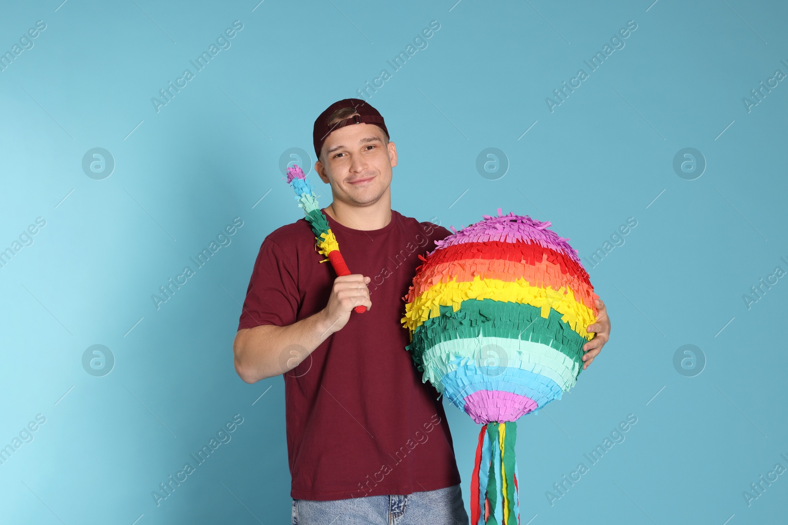 Photo of Happy man with colorful pinata and stick on light blue background