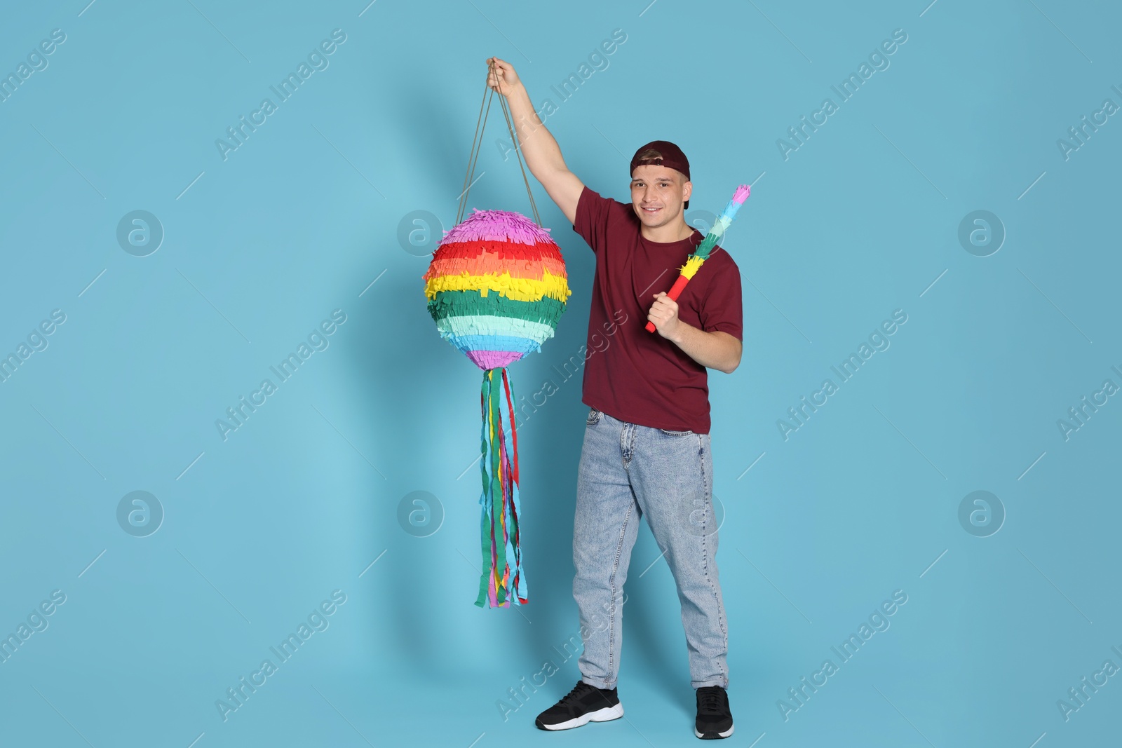 Photo of Happy man with colorful pinata and stick on light blue background