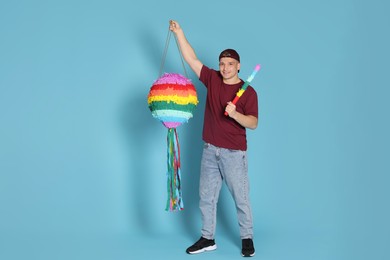 Photo of Happy man with colorful pinata and stick on light blue background