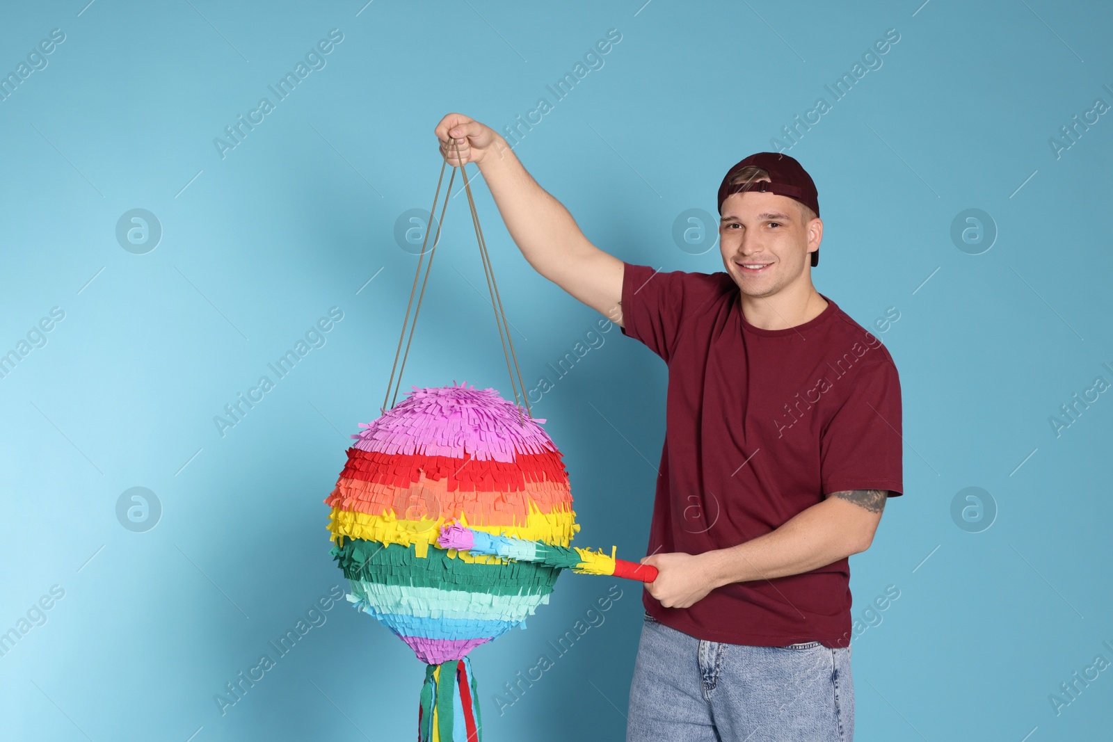 Photo of Happy man breaking pinata on light blue background