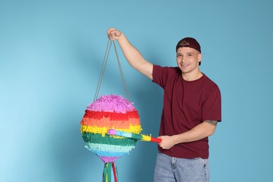 Photo of Happy man breaking pinata on light blue background