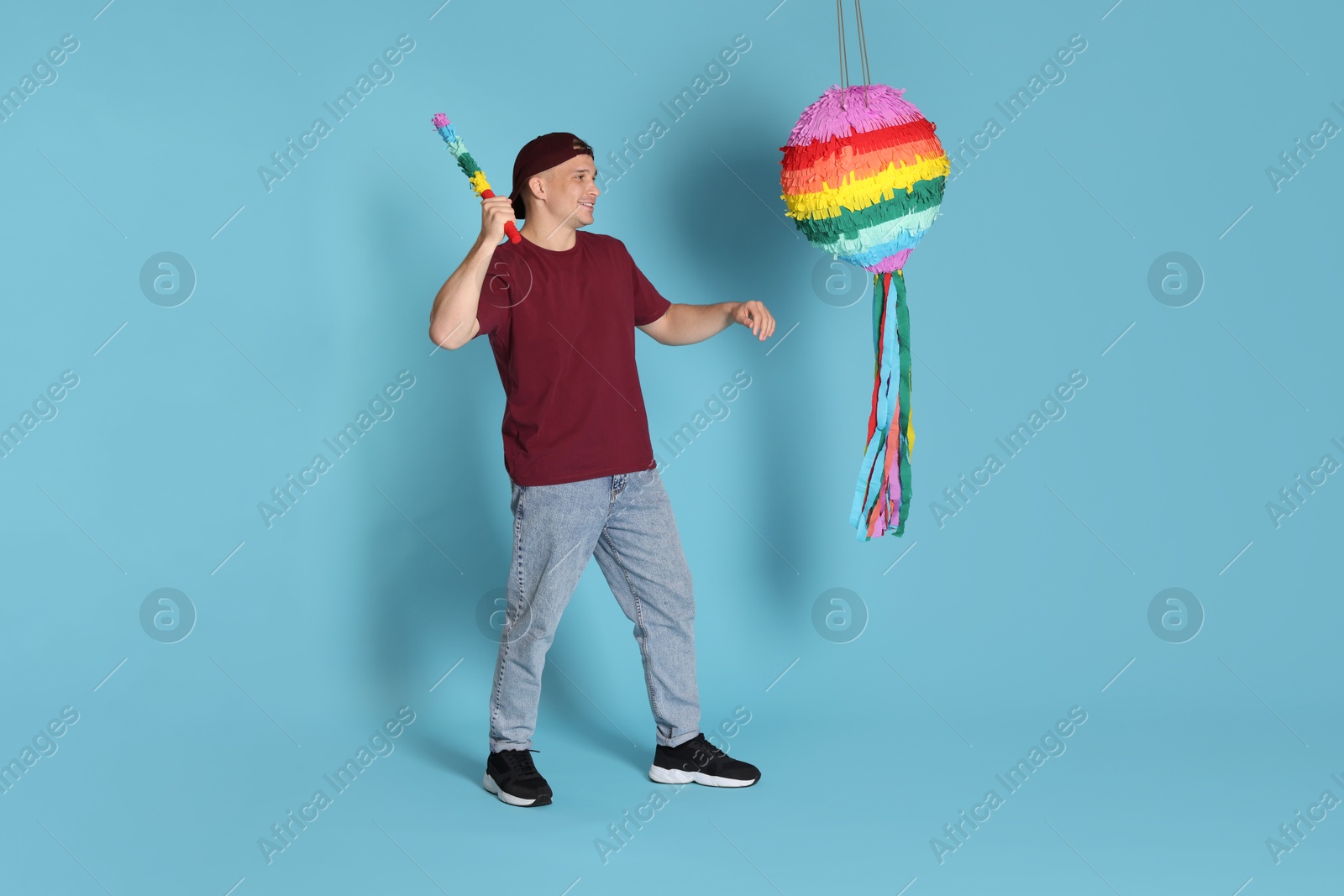 Photo of Happy man breaking pinata on light blue background