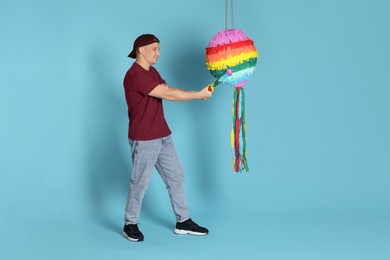 Photo of Happy man breaking pinata on light blue background