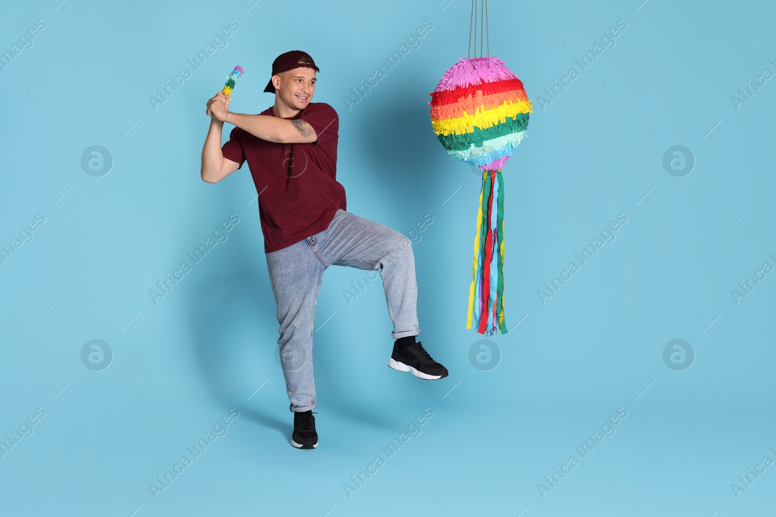 Photo of Happy man breaking pinata on light blue background