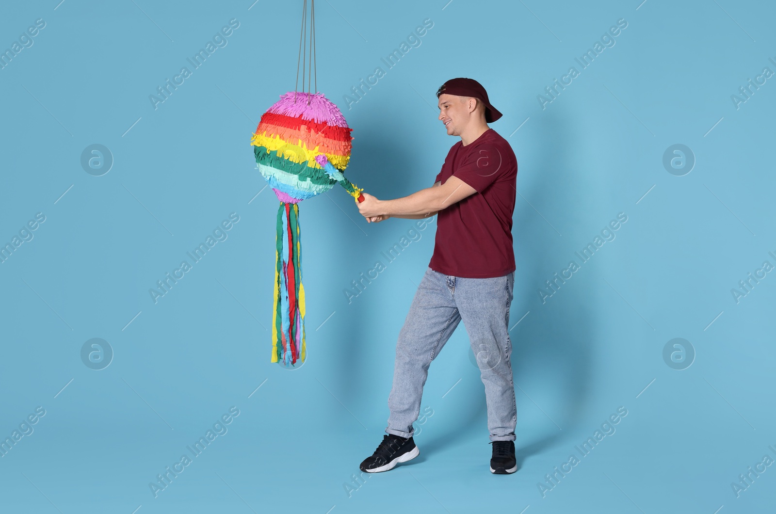 Photo of Happy man breaking pinata on light blue background