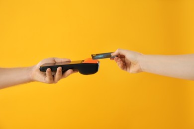 Photo of Man taking payment from client via terminal on yellow background, closeup