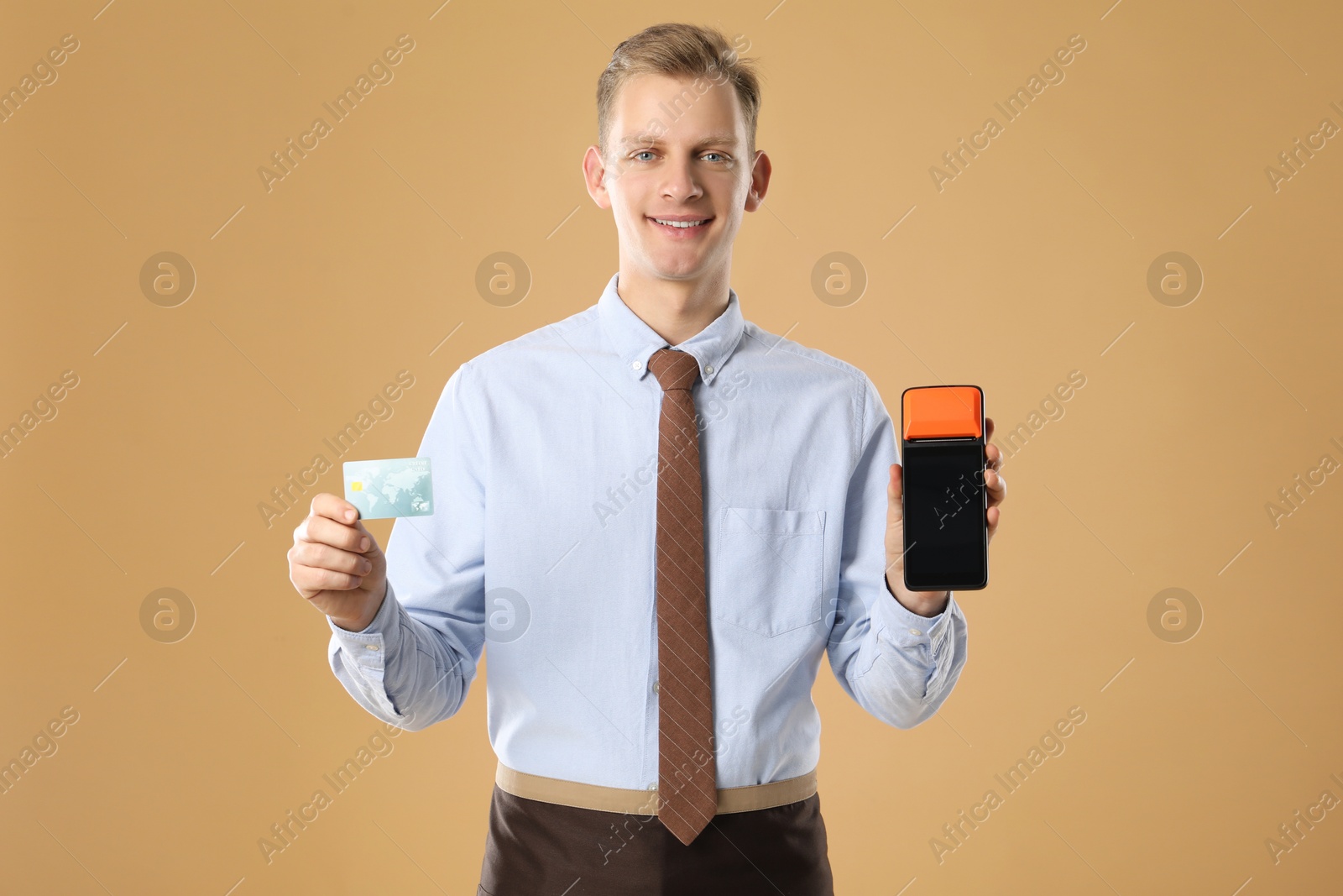 Photo of Happy young man with payment terminal on beige background