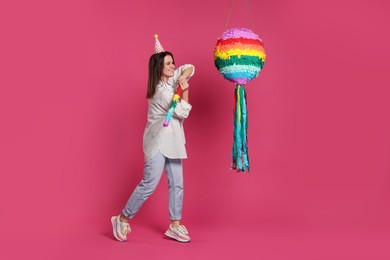 Photo of Happy woman hitting colorful pinata with stick on pink background