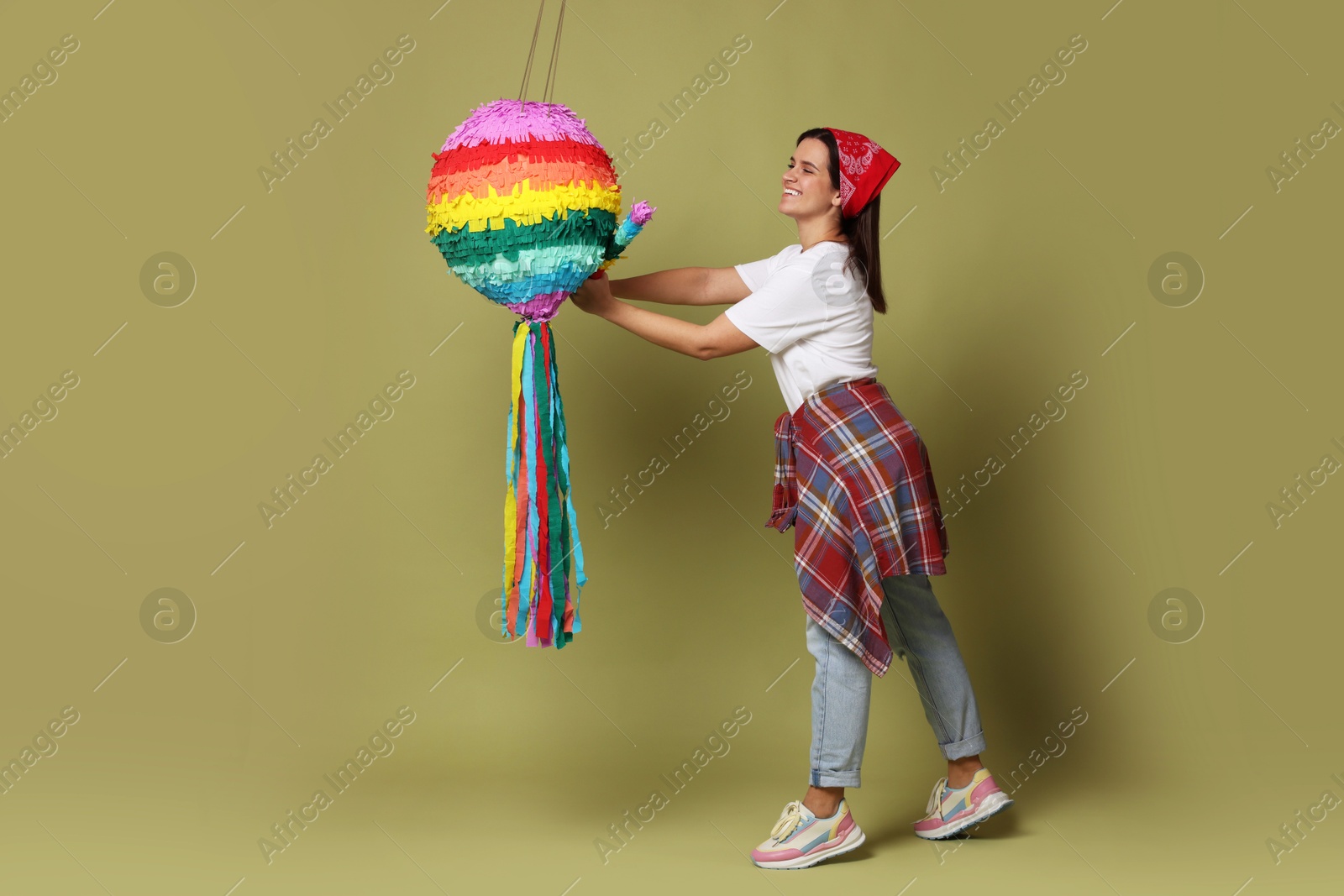 Photo of Happy woman hitting colorful pinata with stick on green background