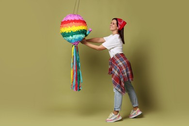 Happy woman hitting colorful pinata with stick on green background