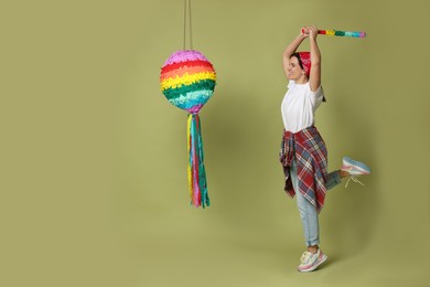 Photo of Happy woman hitting colorful pinata with stick on green background