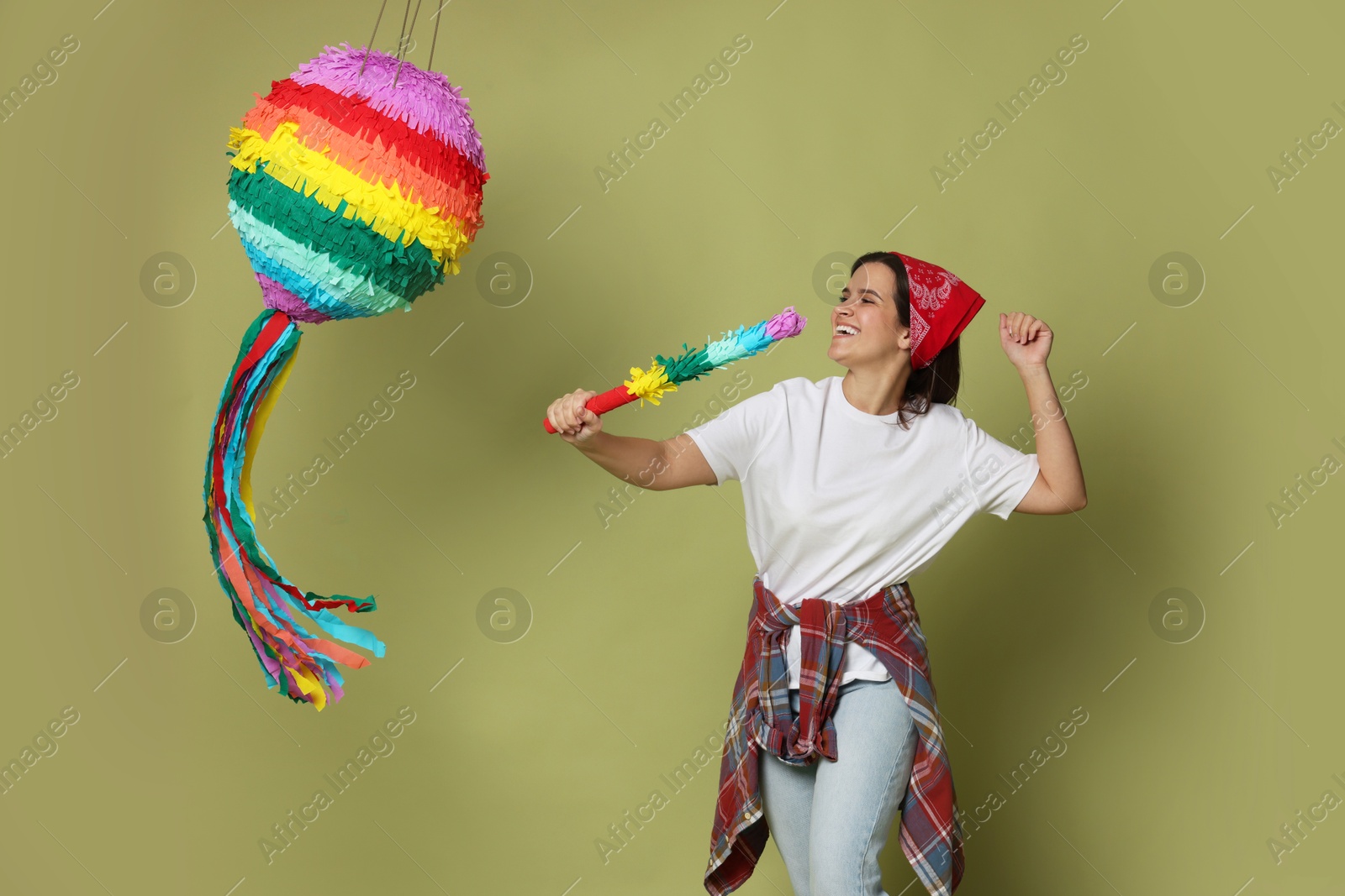 Photo of Happy woman hitting colorful pinata with stick on green background