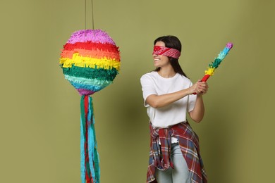 Photo of Woman with tied eyes breaking pinata on green background