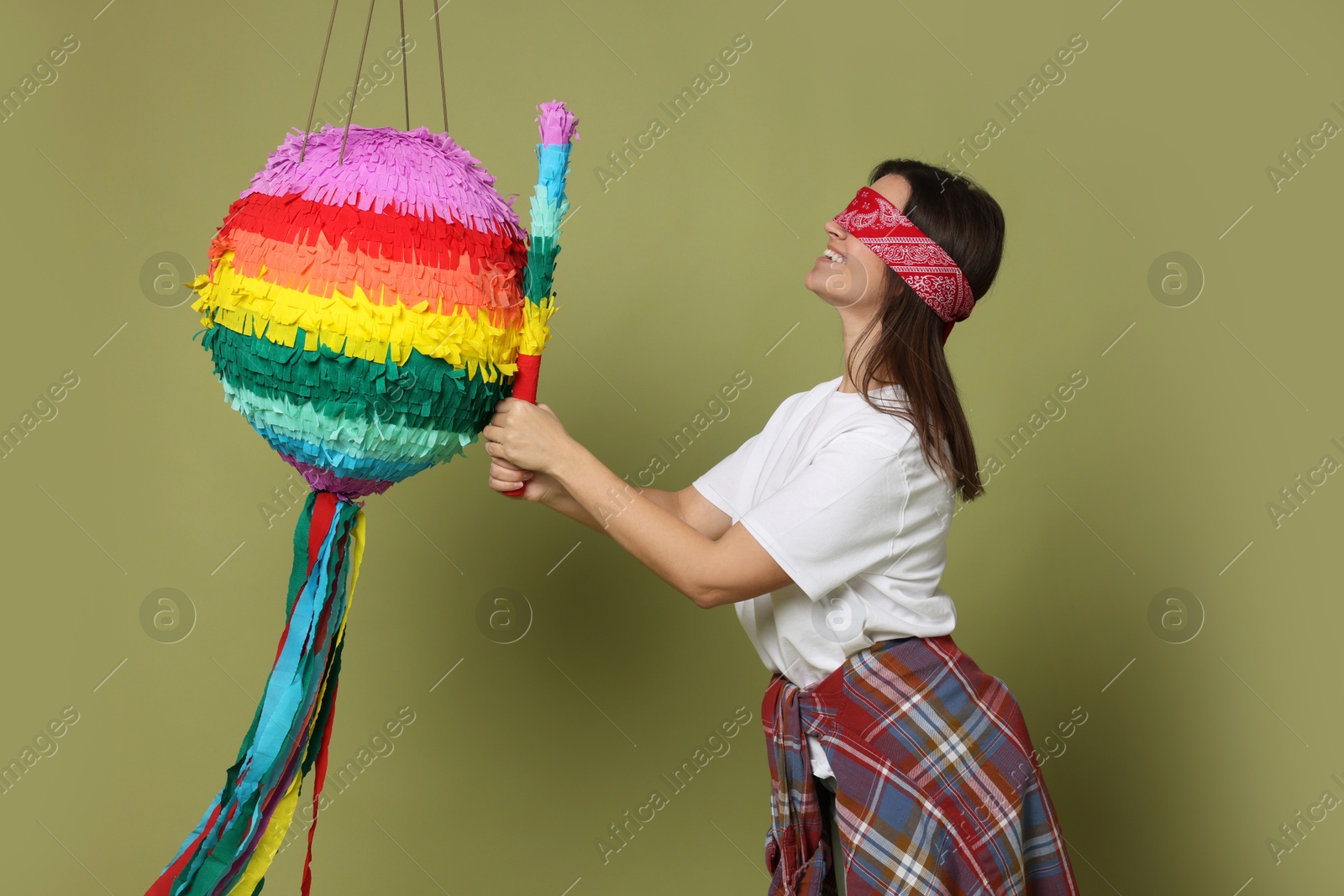 Photo of Woman with tied eyes breaking pinata on green background