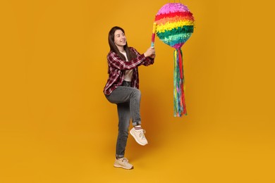 Photo of Happy woman hitting colorful pinata with stick on orange background