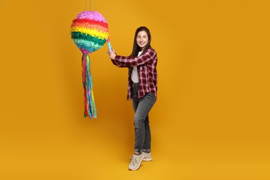 Photo of Happy woman hitting colorful pinata with stick on orange background