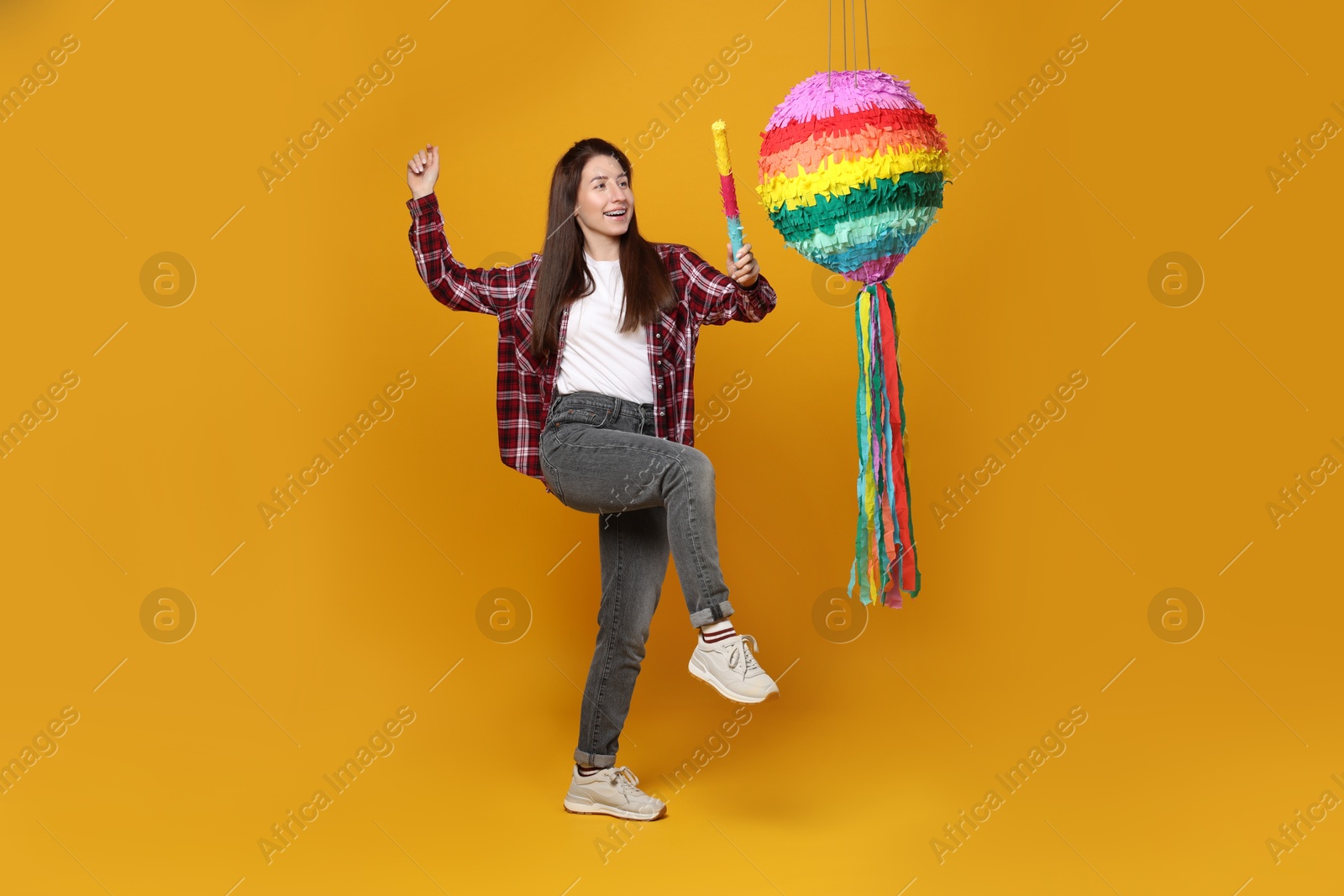 Photo of Happy woman hitting colorful pinata with stick on orange background