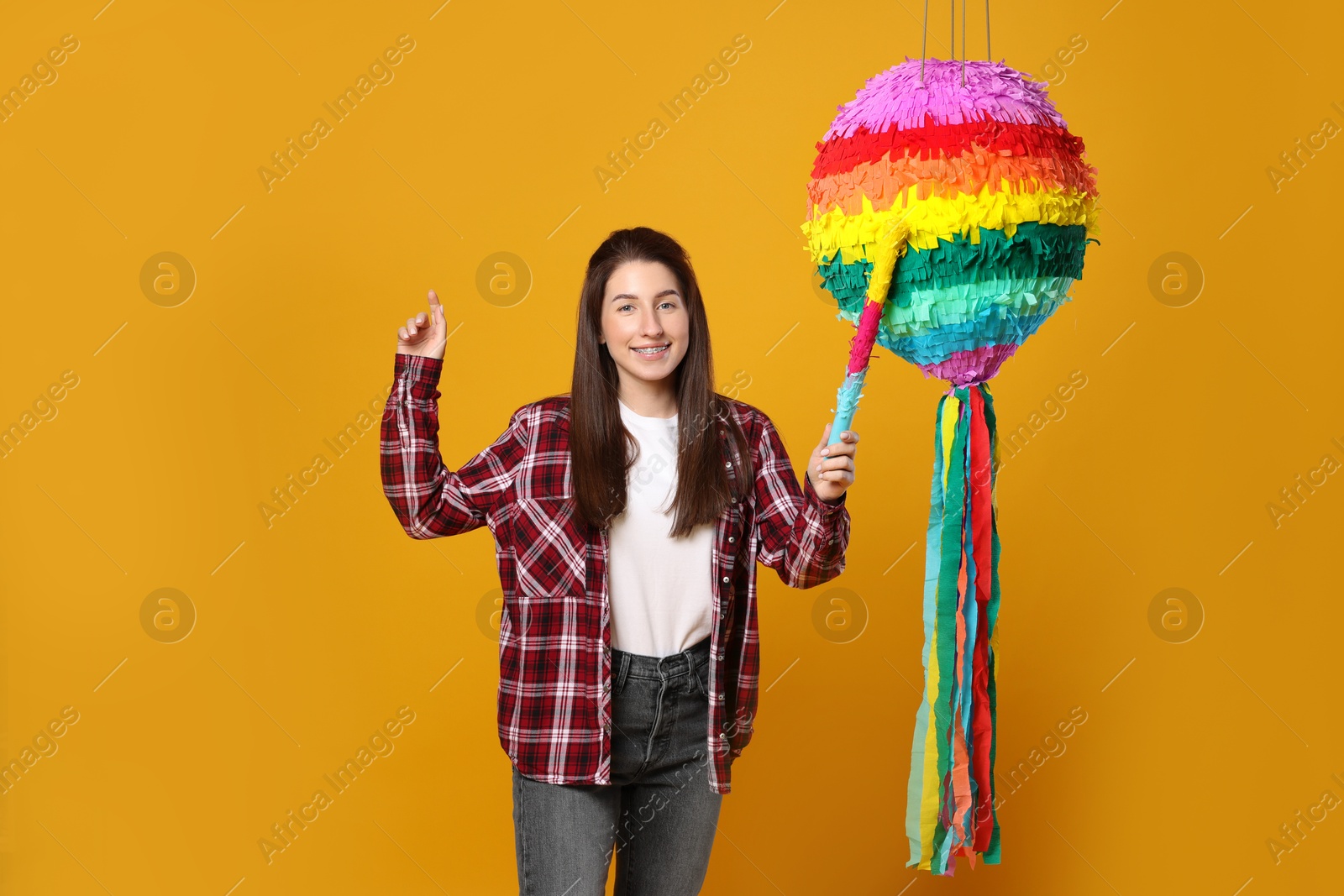 Photo of Happy woman hitting colorful pinata with stick on orange background