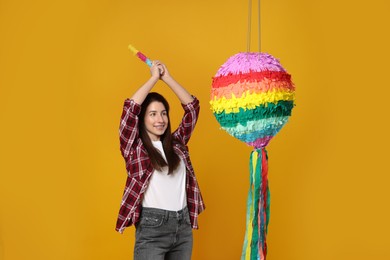 Photo of Happy woman hitting colorful pinata with stick on orange background