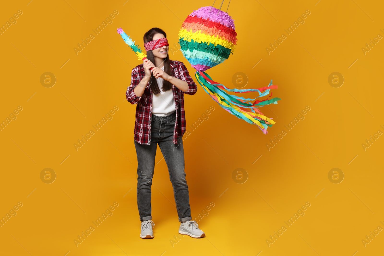 Photo of Woman with tied eyes breaking pinata on orange background