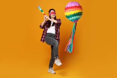 Photo of Woman with tied eyes breaking pinata on orange background