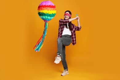 Photo of Woman with tied eyes breaking pinata on orange background