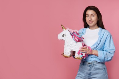 Photo of Woman with unicorn shaped pinata on pink background, space for text