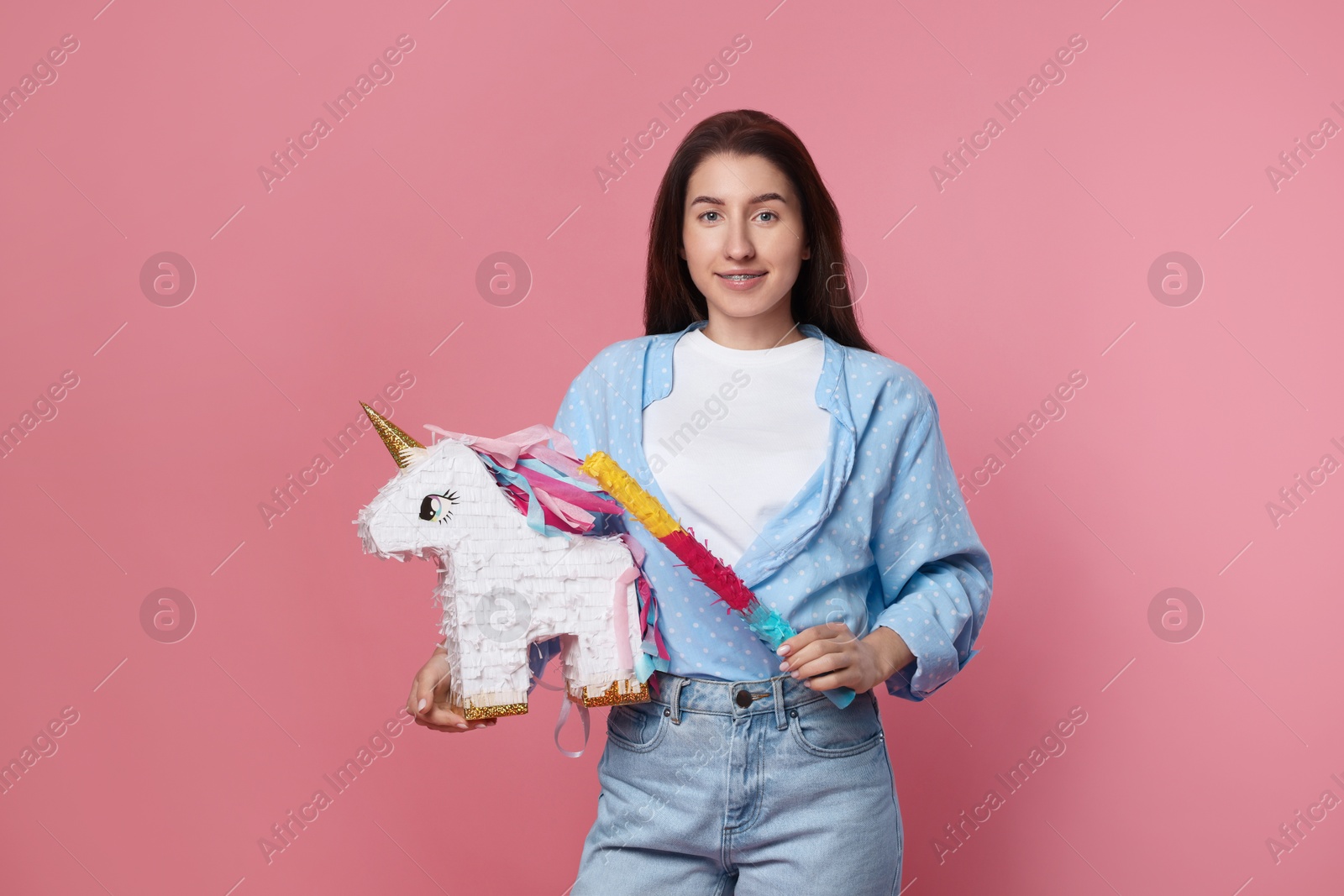 Photo of Happy woman with unicorn shaped pinata and stick on pink background