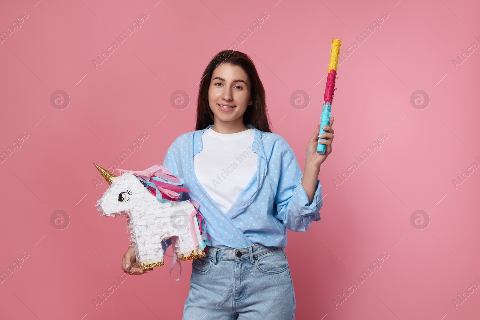 Photo of Happy woman with unicorn shaped pinata and stick on pink background